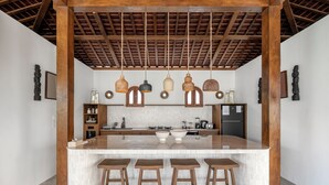 Een moderne keuken met een centraal eiland, houten krukken, hangende pendelverlichting en een betegelde achterwand.