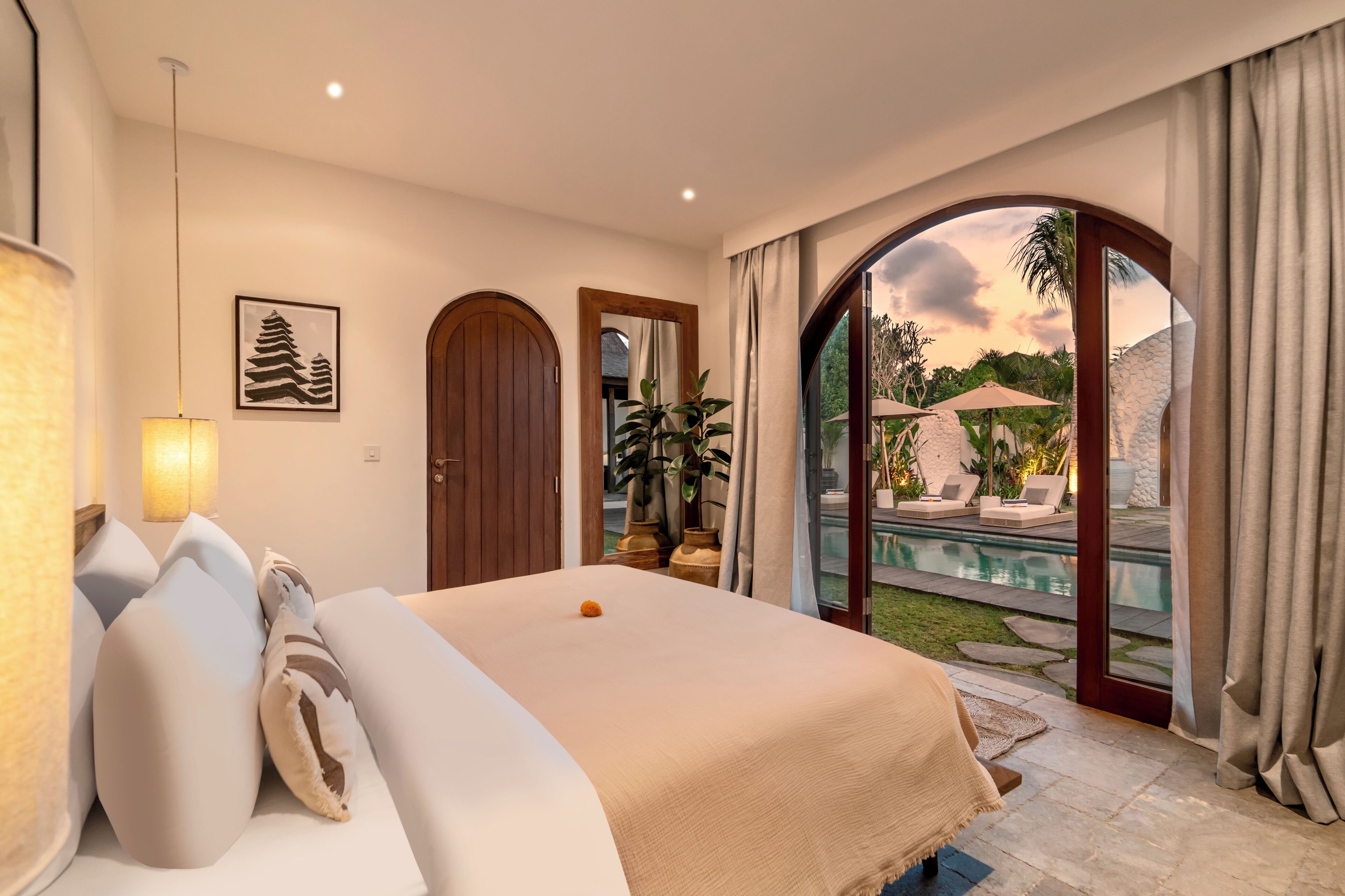 A hotel room with a bed, a large window, and a view of a pool and garden.