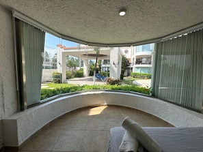 Una habitación con un balcón curvo, una cama y vistas a un patio con piscina y edificios.