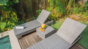 Ein Poolbereich mit zwei Korbstühlen, einem kleinen Tisch mit einem Getränk und üppiger Bepflanzung.