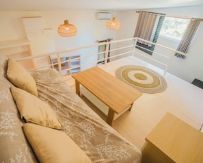 Une chambre à coucher avec un lit, une table en bois, un tapis tissé et un balcon doté d’une balustrade.