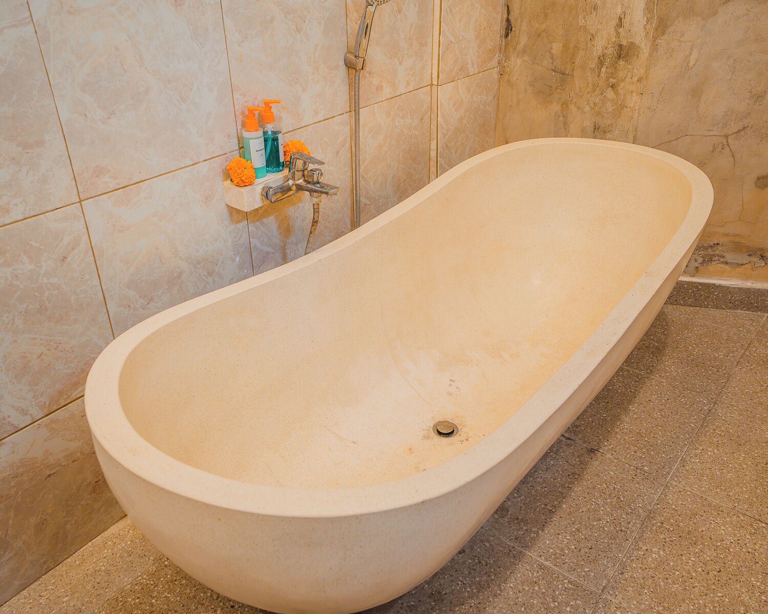 A bathtub in a bathroom with tiled walls, a showerhead, and toiletries on a shelf.