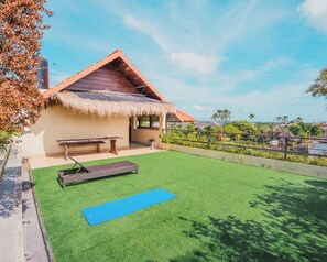 A house with a thatched roof, a patio with a table and bench, and a blue exercise mat on artificial grass.