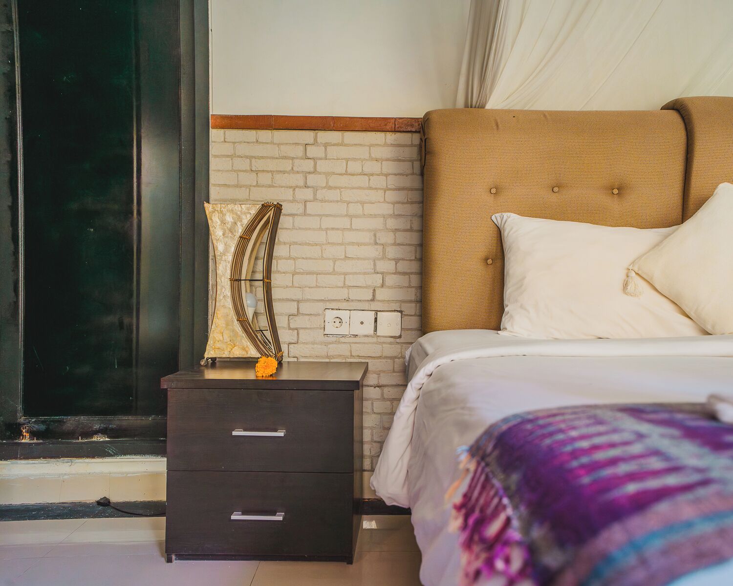 A bedroom with a bed, a nightstand, a mirror, and a brick-patterned wall.