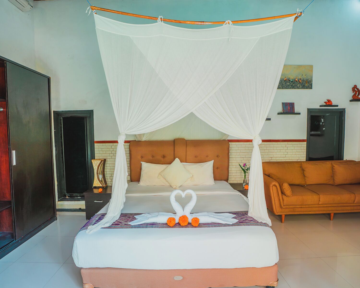 A bed with a canopy, a sofa, a painting, and a door.