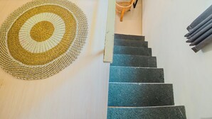 Eine Treppe mit einem Teppich am Fußende, ein Holzstuhl und ein Fenster mit Jalousien.
