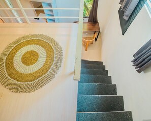 A staircase with a woven rug at the bottom, a wooden chair, and a window with blinds.