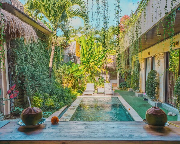 A pool area with lounge chairs, a thatched roof structure, and lush greenery.