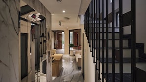 A hallway with a marble floor, a sofa, a plant, and a staircase with black railings. - Luckin Hotel (Ho Chi Minh City)