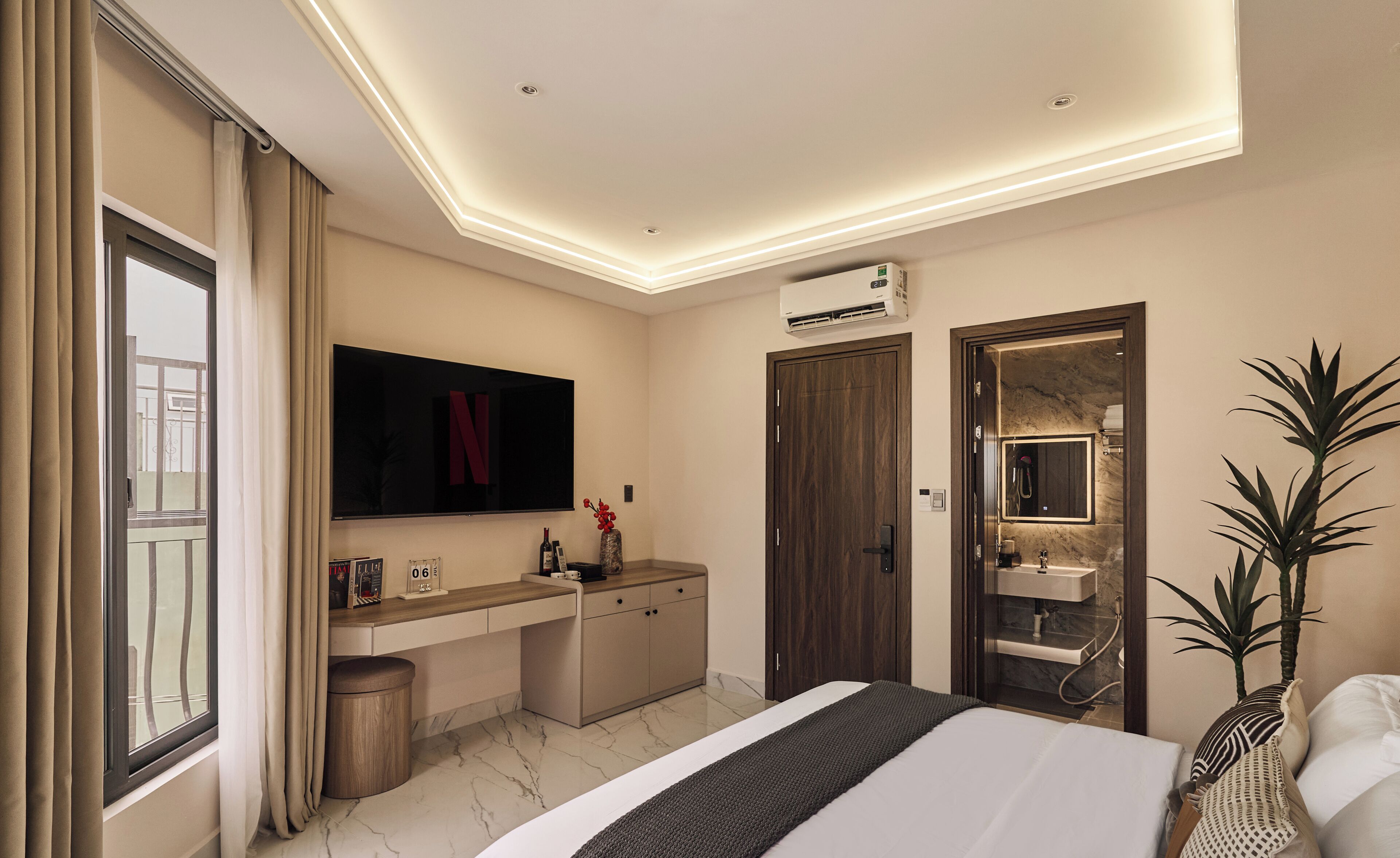 Habitación de hotel con cama, escritorio, tocador con espejo, ventana con cortinas y equipo de aire acondicionado.