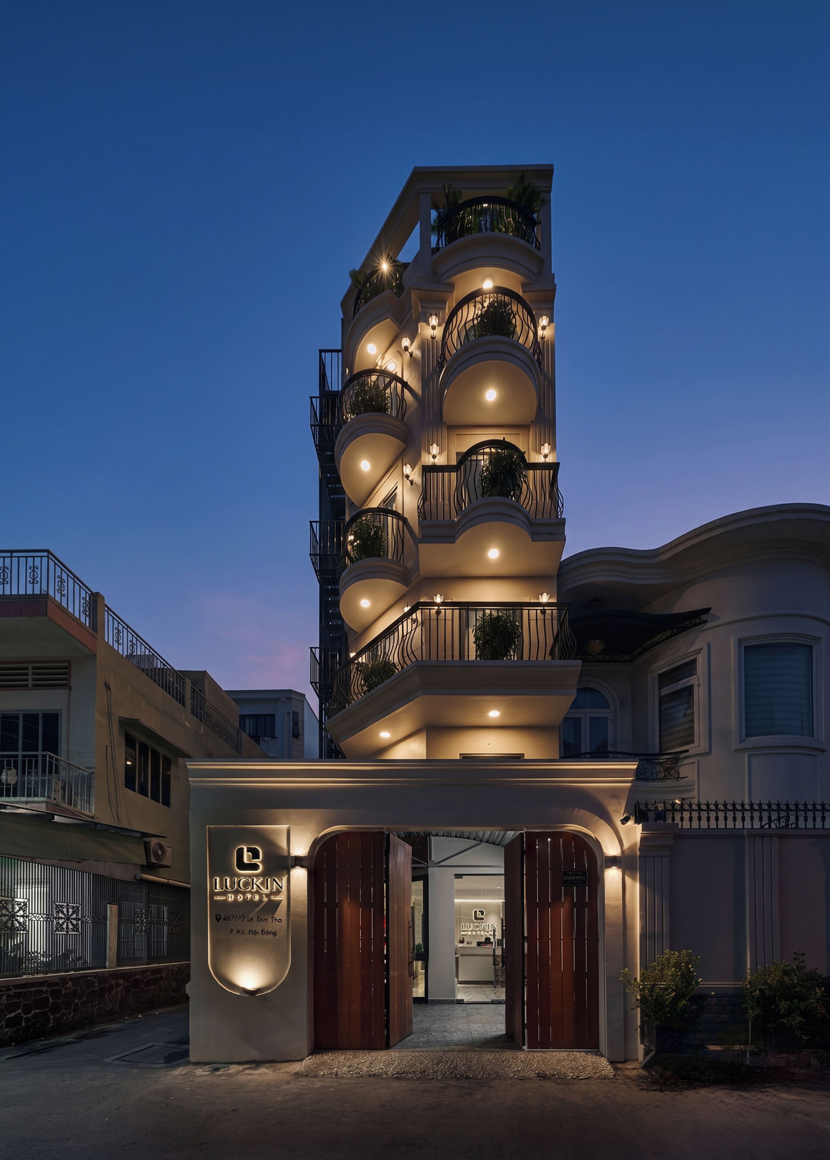 Un hotel de varios pisos con un diseño moderno, que cuenta con balcones con barandillas y plantas en macetas.