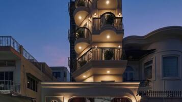 Un hotel de varios pisos con un diseño moderno, que cuenta con balcones con barandillas y plantas en macetas.