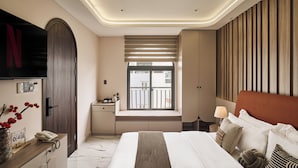 A modern hotel room with a large bed, a desk with a telephone, a window with blinds, and a TV mounted on the wall. - Luckin Hotel (Ho Chi Minh City)