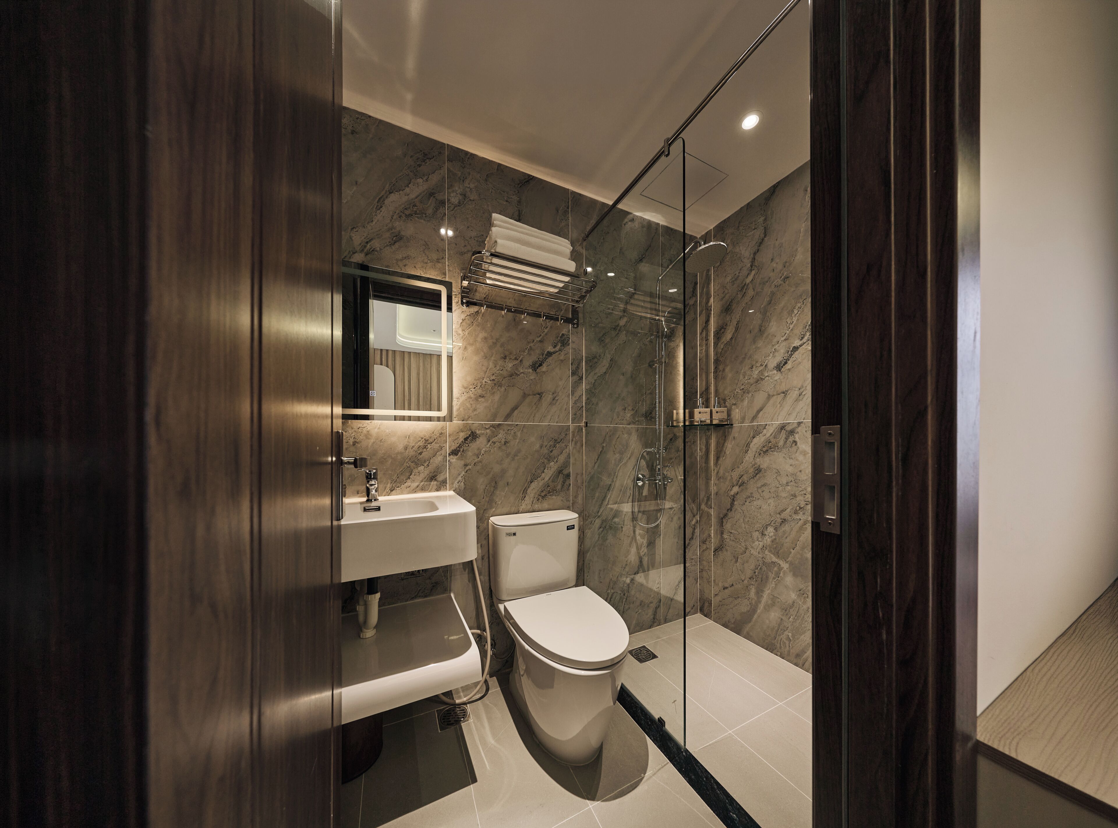 Un baño moderno con cabina de ducha de vidrio, un lavabo blanco y un inodoro.