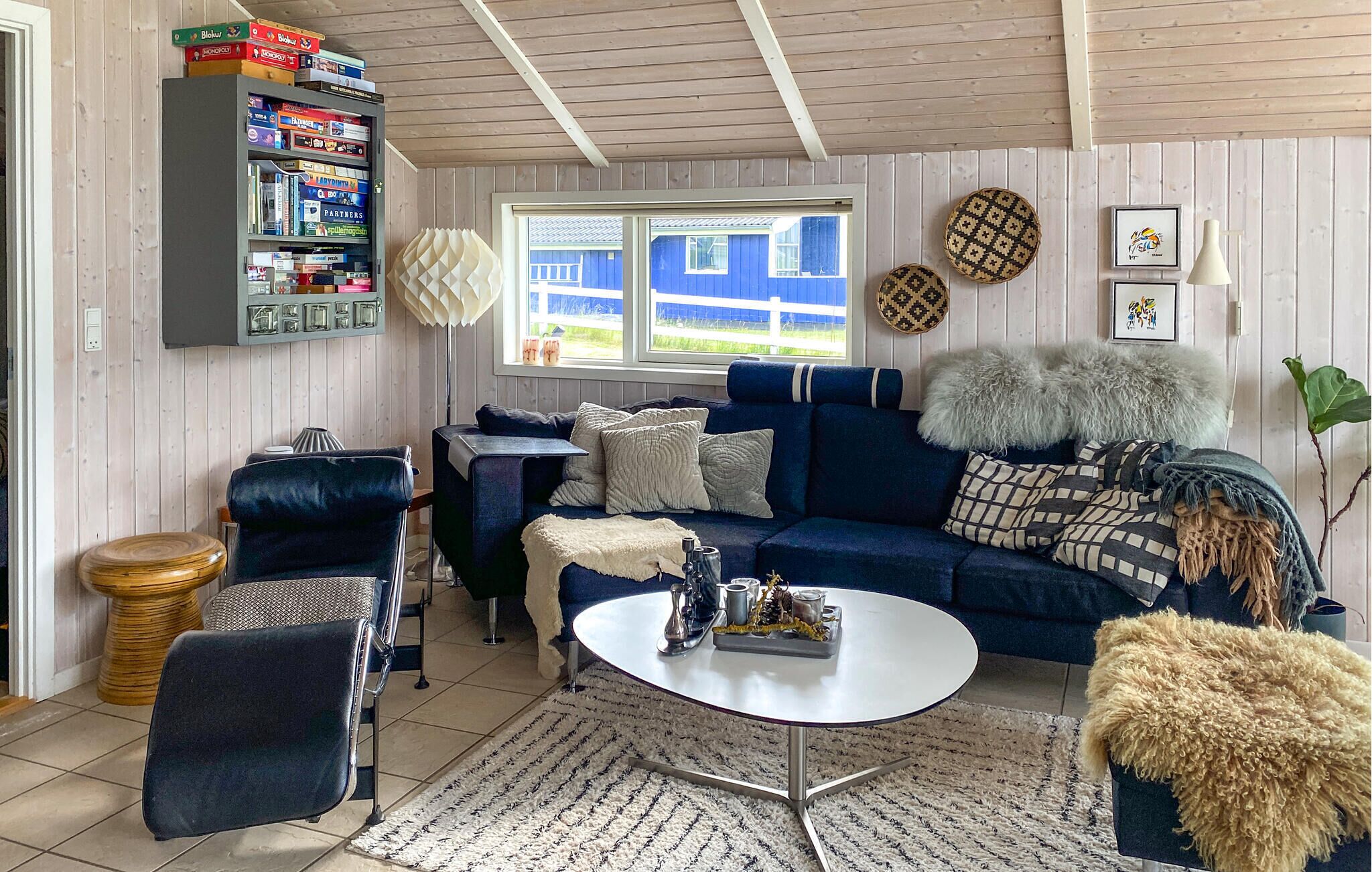 Een woonkamer met een blauwe bank, een salontafel, een boekenkast en uitzicht op buiten.