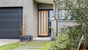 A modern building with a brick facade, a wooden-framed door, and a black garage door. - Tea Tree Poolside Escape (Inverloch)