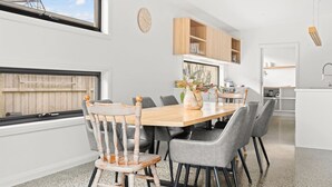 A modern kitchen with a wooden dining table, grey chairs, a vase with flowers, and a clock on the wall. - Tea Tree Poolside Escape (Inverloch)