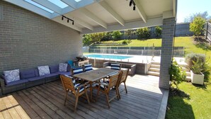 A covered patio with a pool, wooden furniture, and a brick wall. - Tea Tree Poolside Escape (Inverloch)
