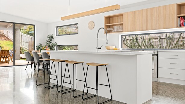 A modern kitchen with a central island, bar stools, a window, and a view of the outdoors. - Tea Tree Poolside Escape (Inverloch)