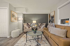 Ein Wohnzimmer mit rundem Couchtisch, zwei Sesseln, einer Couch, einem Beistelltisch mit Lampe und einem Blumentopf.