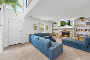 A living room with a sectional sofa, fireplace, bookshelf, and a door. - World Cup Home Base | 3BR + King Suite (Shawnee)