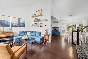 A spacious living area with a piano, blue sofa, and a dining area with a table and chairs. - World Cup Home Base | 3BR + King Suite (Shawnee)