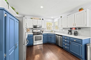 A kitchen with white and blue cabinets, stainless steel appliances, and a wooden floor. - World Cup Home Base | 3BR + King Suite (Shawnee)
