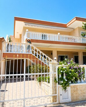 Uma casa de dois andares com varanda, portão e escada.