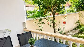 Un patio exterior cubierto con una mesa y sillas, rodeado de vegetación y vistas a una zona residencial.