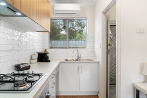 A modern kitchen with white cabinets, a gas stove, a sink, and a window with a view of trees. - FLO at Henley Beach: Beach, Brunch & Shopping (Henley Beach)
