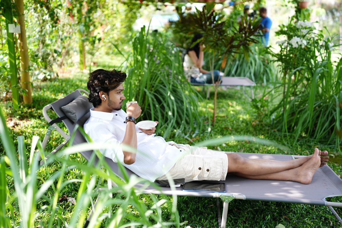 Una persona recostada en una silla de jardín, rodeada de césped y plantas.