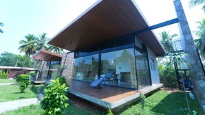 Een modern huis met een houten terras, grote glasramen en een stenen pilaar.