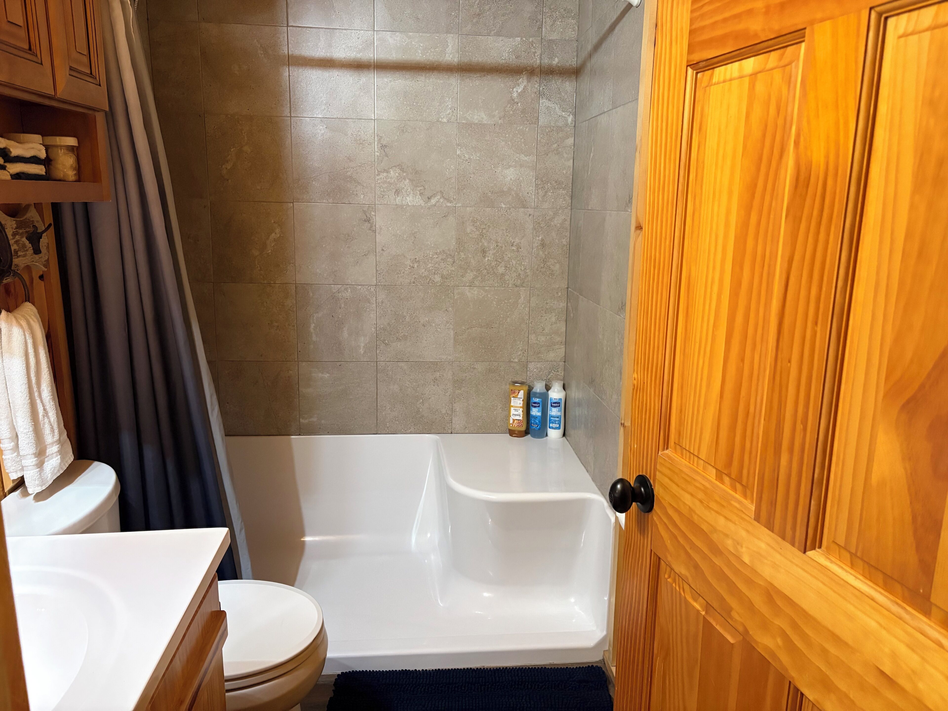 A bathroom with a bathtub, toilet, wooden cabinets, and a shower curtain.