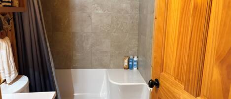 A bathroom with a bathtub, toilet, wooden cabinets, and a shower curtain.