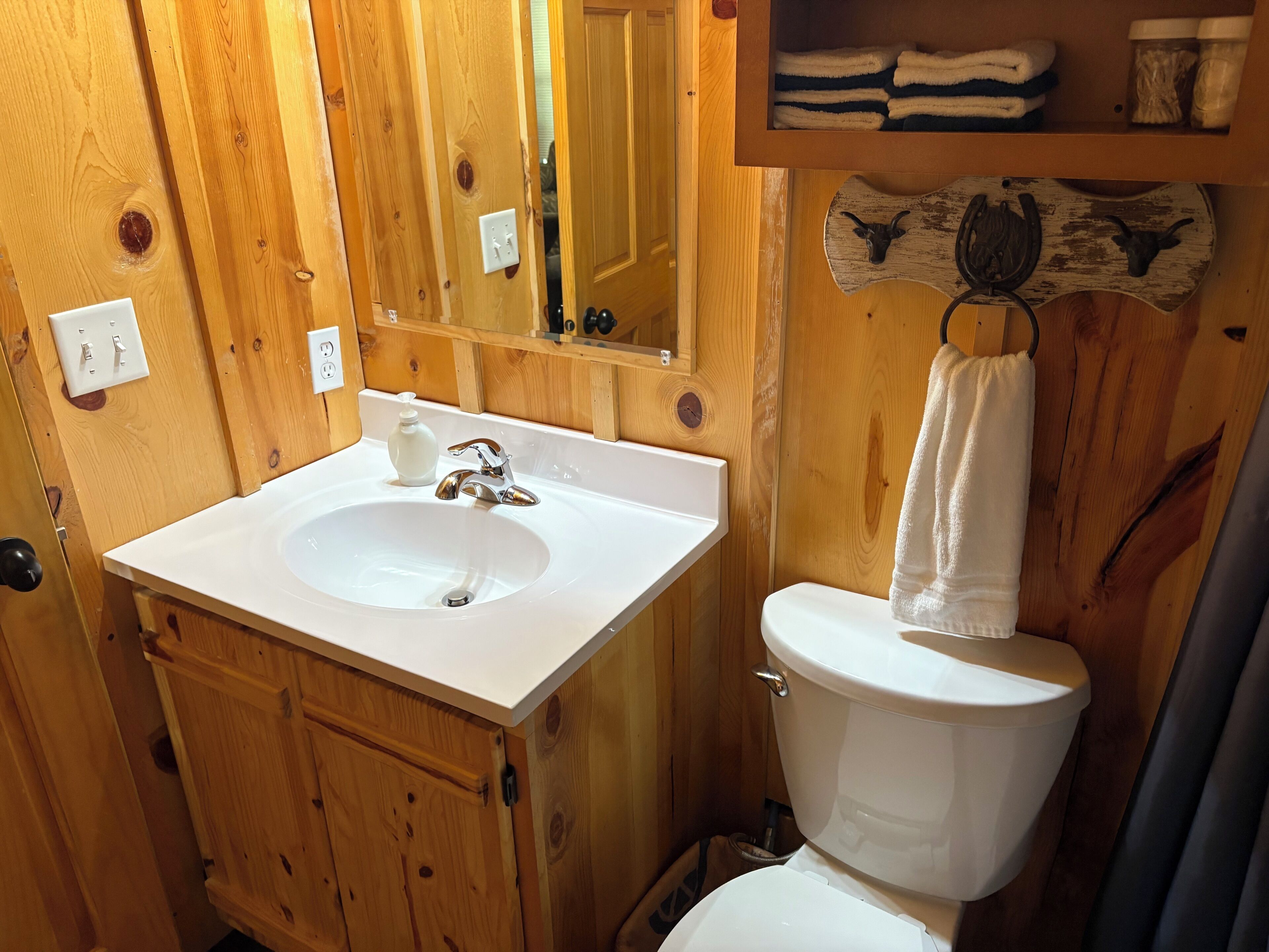 A wooden bathroom with a white sink, a mirror, a toilet, and a towel rack.