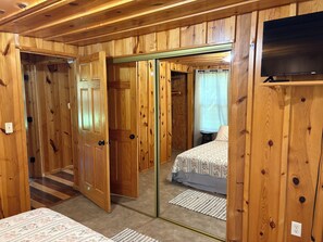 Ein Zimmer mit Holzwänden, einem Bett, einem Fernseher und einem Spiegel.
