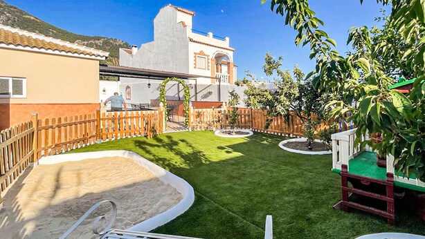Un jardín bien cuidado con piscina, cerca de madera y un edificio con techo de tejas.