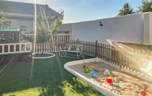 A fenced outdoor play area with sand, a bench, and a small tree. - Vivienda Turistica La Gallomba (Rute)