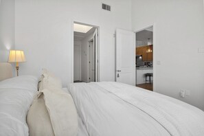 Ein Schlafzimmer mit einem Bett, einer Nachttischlampe und einer offenen Tür zu einer Küchenzeile.