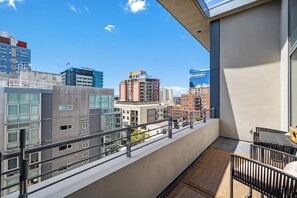 Ein Balkon mit Blick auf Stadtgebäude, einer Betonwand und einem Metallgeländer.