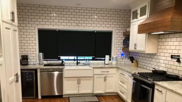 Eine Küche mit weißen Schränken, einem Edelstahl-Geschirrspüler, einem Herd und einem Fenster über der Spüle.