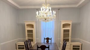 Ein Esszimmer mit einer Chandelüster, einem Holztisch, Stühlen und eingebauten Bücherregalen.