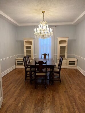 Ein Esszimmer mit einer Chandelüster, einem Holztisch, Stühlen und eingebauten Bücherregalen.