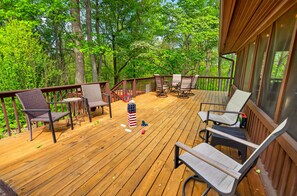 A wooden deck with outdoor furniture, including chairs and a table, surrounded by trees. - Welcome to M'Hollow, Cozy Cabin, Private Hot Tub, WiFi, and Screened in Porch (Logan)