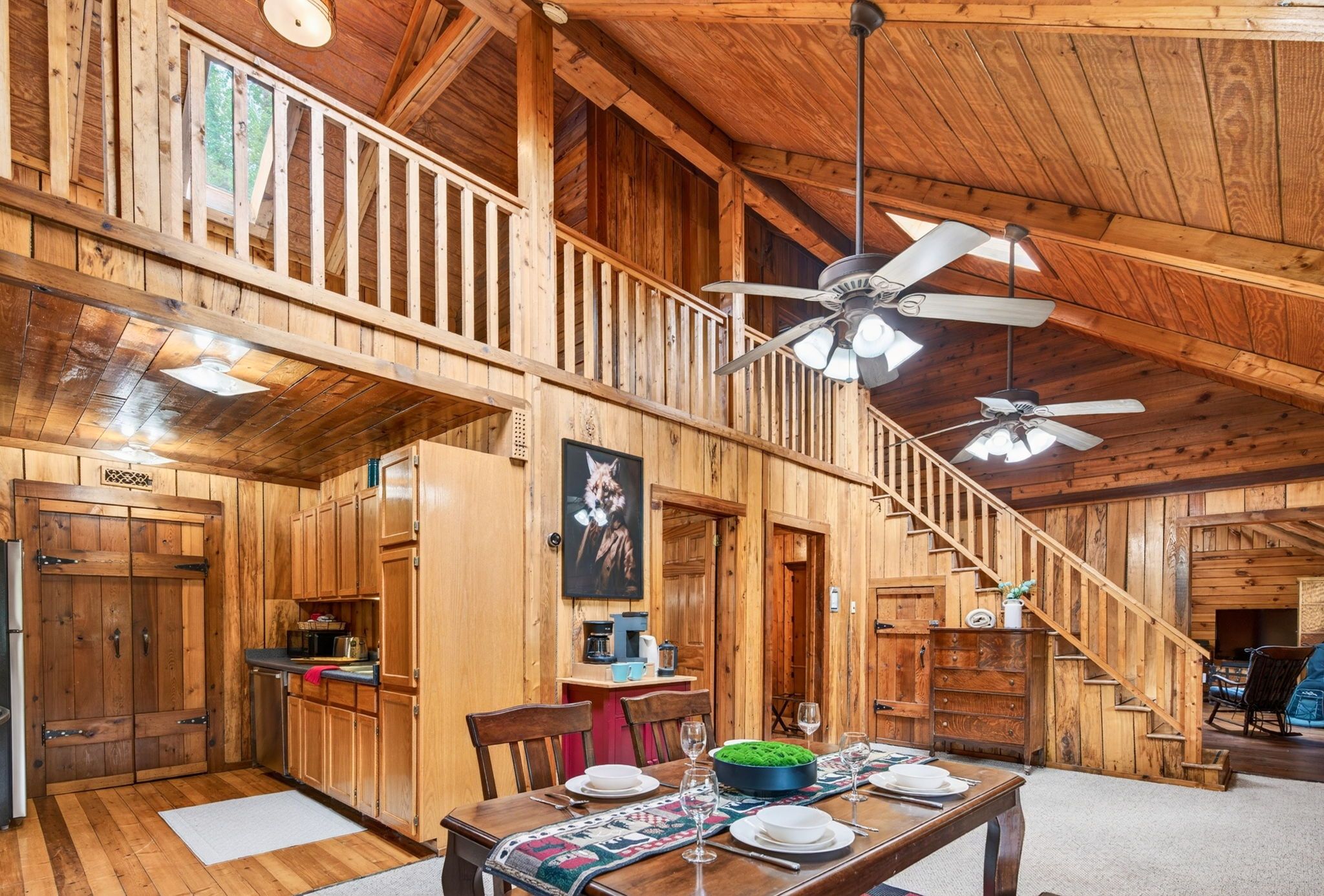 A wooden cabin interior with a dining area, kitchen, and staircase.