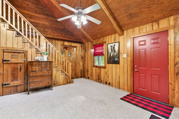 Un intérieur en bois avec un escalier, une porte rouge et un ventilateur de plafond.