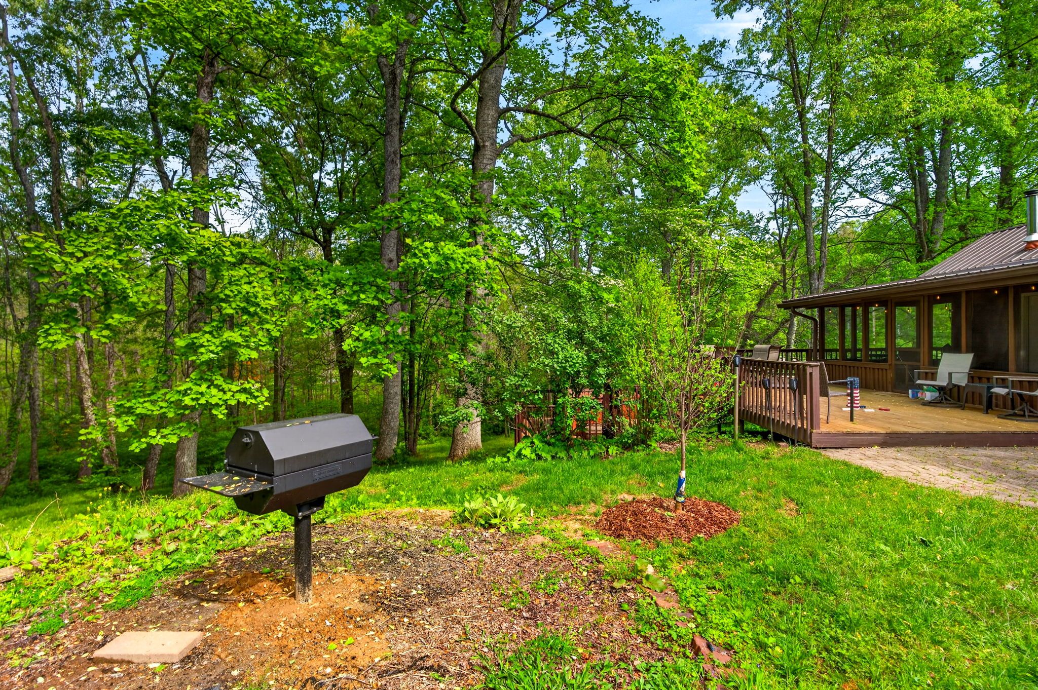 A covered outdoor seating area with a barbecue grill and a small tree in the foreground.