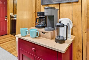 Une petite cuisine équipée d’une machine à café, d’une cafetière et de deux tasses sur un plan de travail en bois.