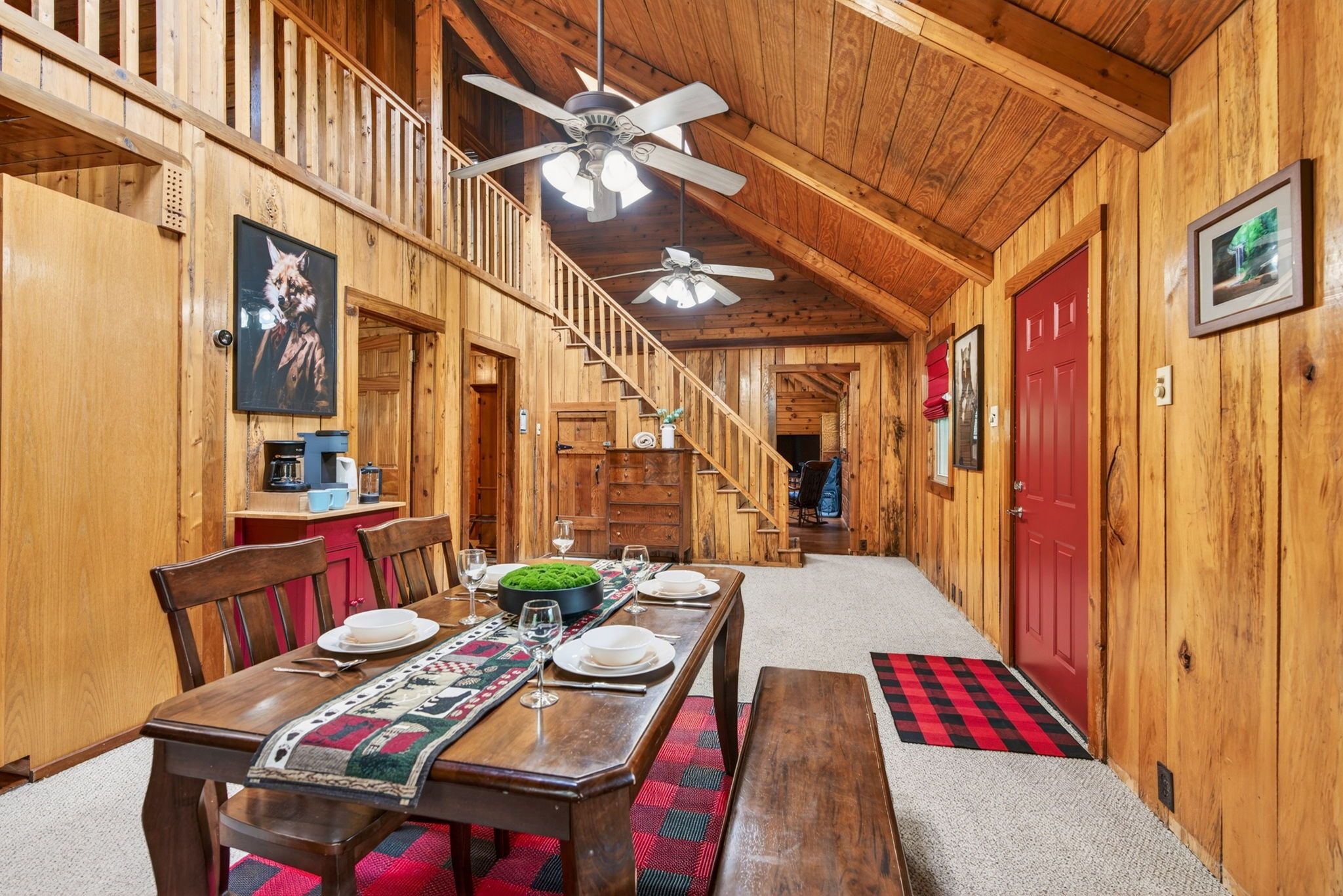 Un intérieur en bois avec une table à manger dressée pour quatre personnes, un escalier et une porte rouge.