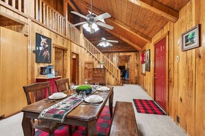 Un intérieur en bois avec une table à manger dressée pour quatre personnes, un escalier et une porte rouge.